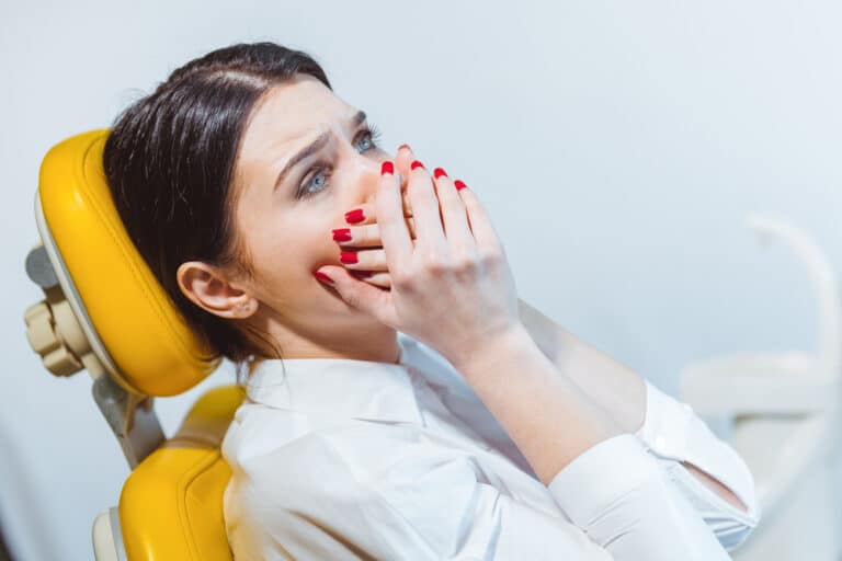 Woman in dentist chair, scared of costs for fixing teeth.