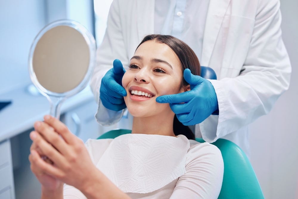 A happy patient looking in the mirror after a smile makeover at the dentist’s
