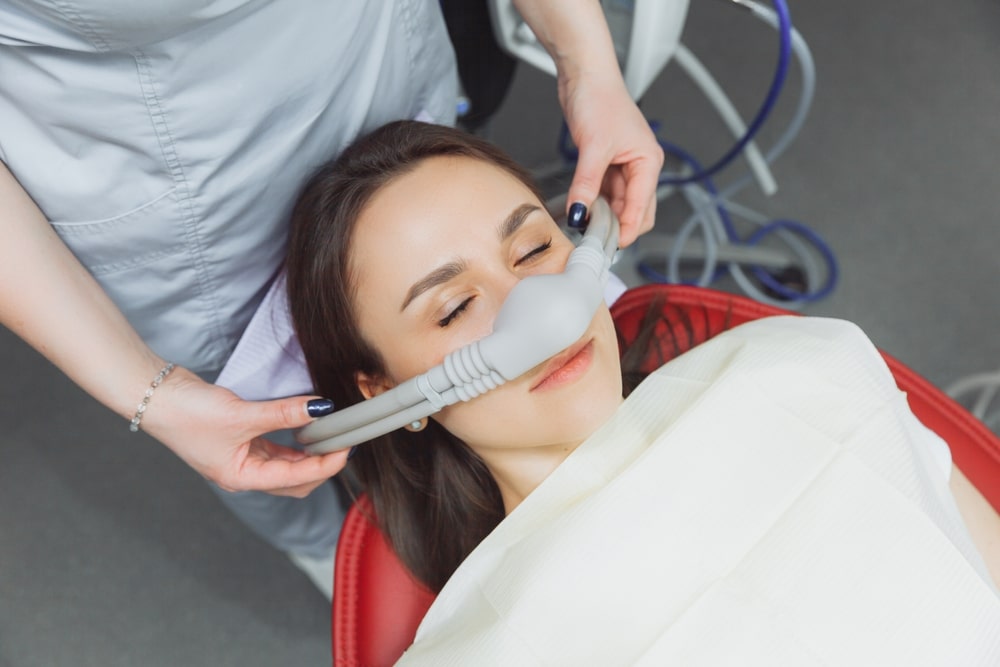 A dentist putting an inhalation sedative mask on her female patient