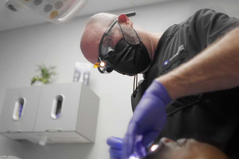 Dental patient smiling while the dentist holds a mirror to show finished treatment.