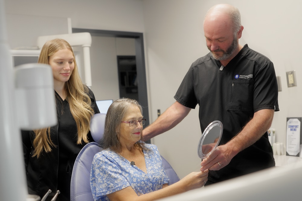Dentist explaining implant-supported bridge treatment using a jaw model during a patient consultation.